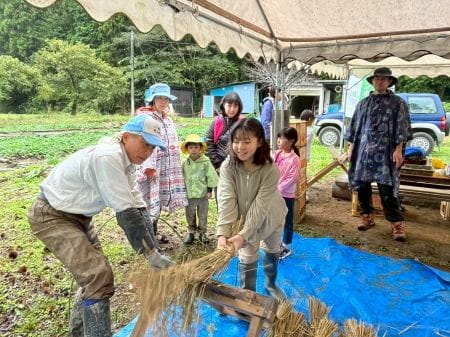 笑顔を見せて脱穀に挑戦する女性